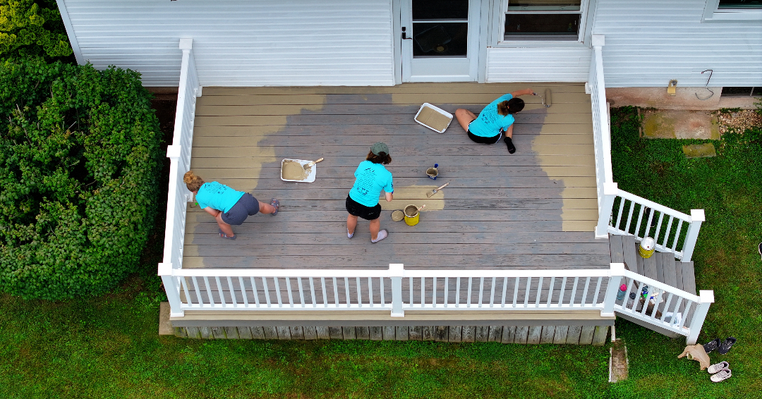 three women painting a wooden terrace 